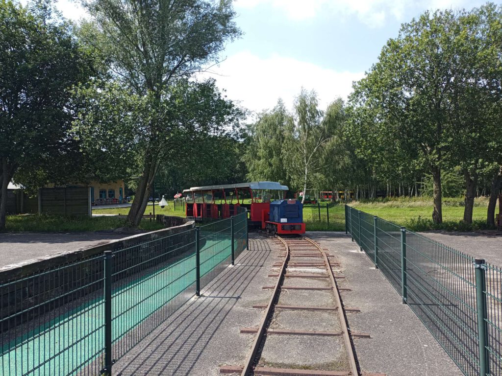 Op het spoor staat een blauwe locomotief met daarachter een rood-witte wagon om passagiers mee te vervoeren.