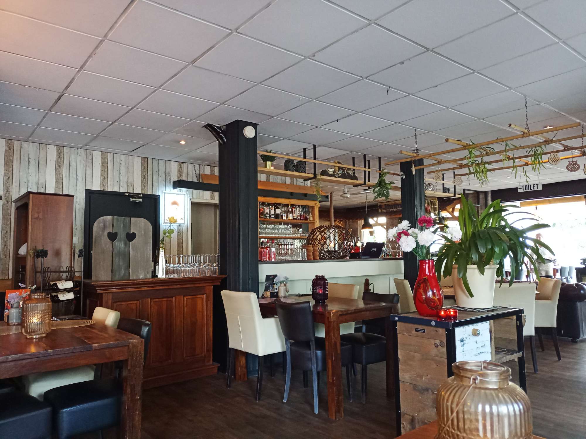 Het interieur met een wit systeemplafond zonder verlichting, met bruine tafels en stoelen naar de bar in dezelfde tinten met reclamemateriaal.