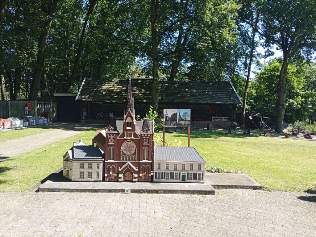 Een miniatuur van de katholieke kerk in Oosterhout, met oranje-rode wanden en en puntdak of spitse toren. Naast de kerk staan witte panden. 