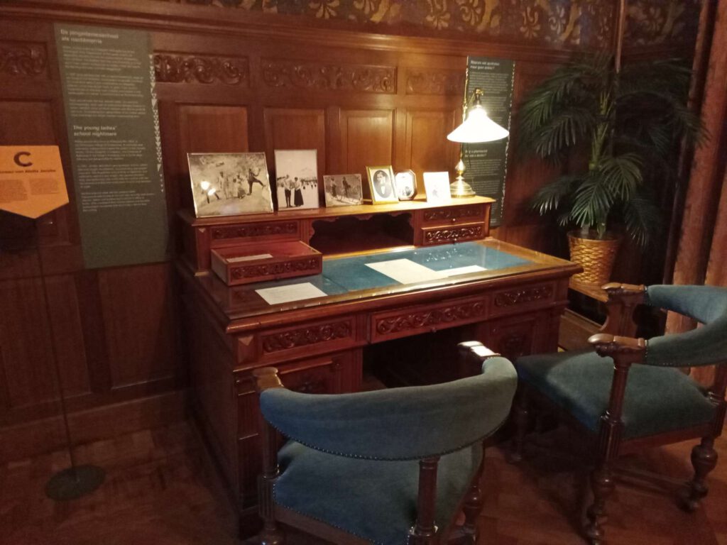 Het bureau is gemaakt van donkerbruin hout. OP het bureau is blauwe stof gemaakt. De stoelen erbij zijn van hout in ook een donkerbruine tint, de rugleuning en zitvlak zijn gestoffeerd met blauwe stof.