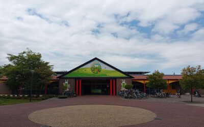 Een plein met op de grond een cirkel. Het entreegebouw heeft en puntdak met in het groen een achtergrond, daarvoor staat Verkeers- en Attractiepark Duinen Zathe.