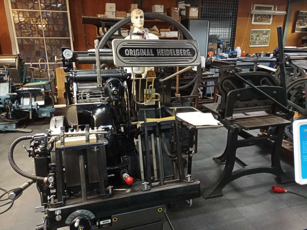 Een heidelberg drukmachine met cillinderpersen. De machine was een nieuwe uitvinding begin 20e eeuw. De machine kon niet alleen drukken, maar ook materiaal bewerken om te vouwen of om bv. een perforeerlijn aan te brengen. Papieren werden middels het opzuigen van de ene kant naar de andere kant overgeheveld. 