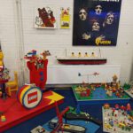 Op de foto staan verschillende bouwwerken van Lego en het lego logo. De bouwwerken die hier te zien zijn onder andere een portret van Queen, een trommel, een clown, een boot in een vaargeul en de titanic.