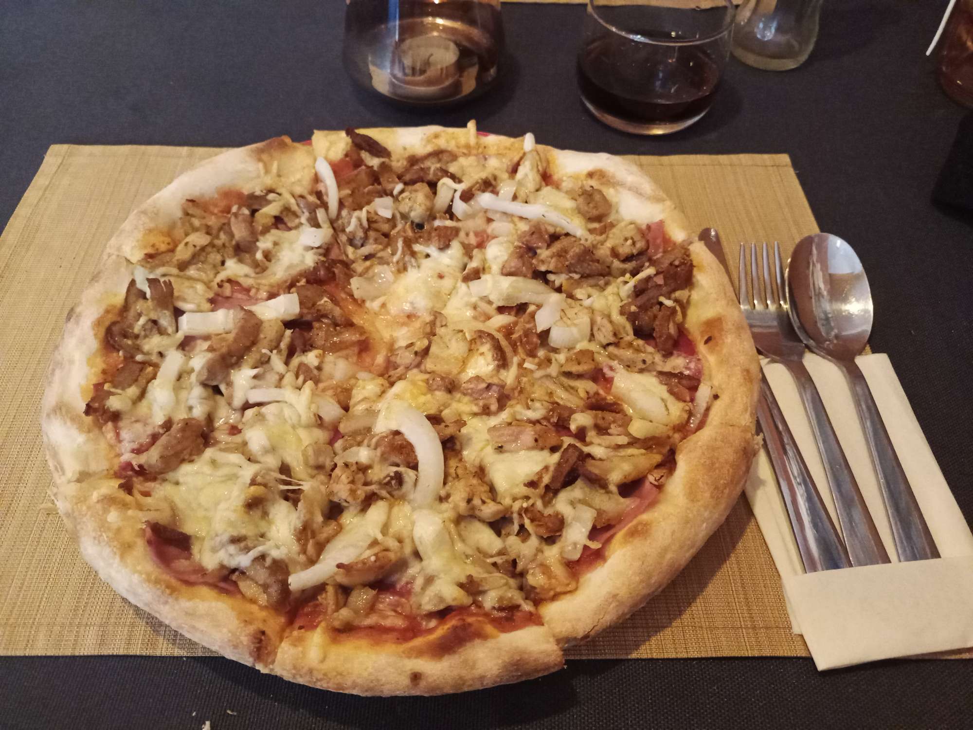 Op een bord ligt een pizza met diverse soorten vlees, uien en brie.
