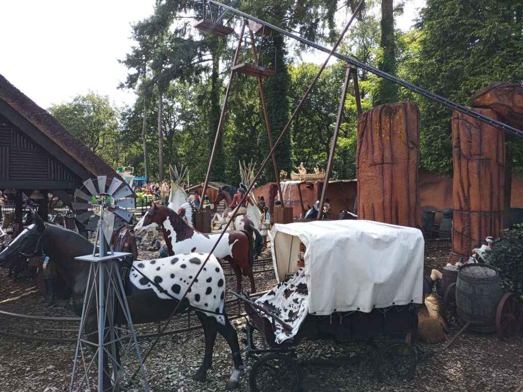 Op de voorgrond een standbeeld/pop van een paard, met daarachter een huifkar, ook staat er een windmolentje, verder naar achteren staan meer paarden en standbeelden van indianen.