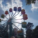 Een reuzenrad tegen de zon in gefotografeerd, met daarboven een blauwe hemel met enkele wolken en felle zon.