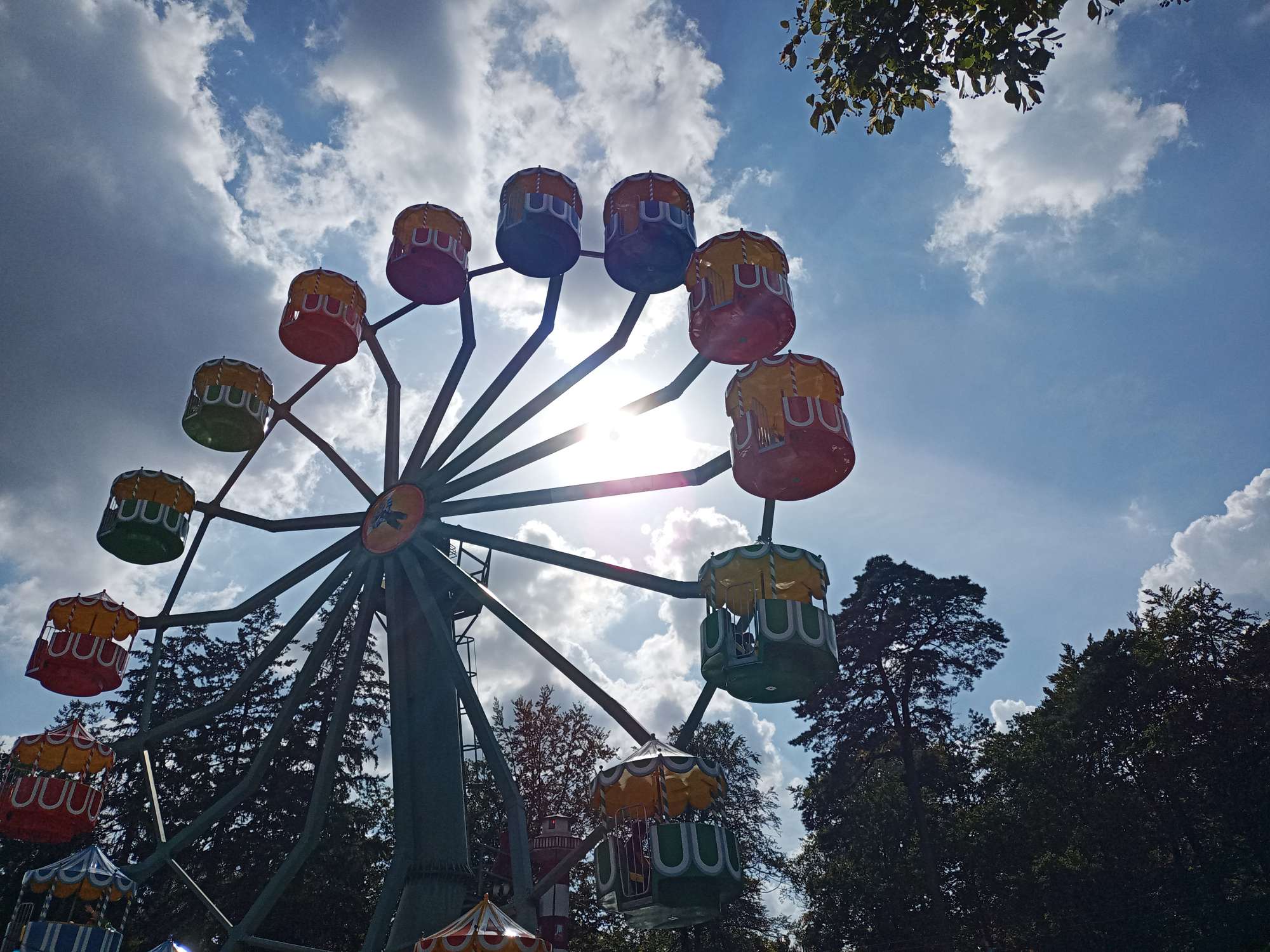 Een reuzenrad tegen de zon in gefotografeerd, met daarboven een blauwe hemel met enkele wolken en felle zon.