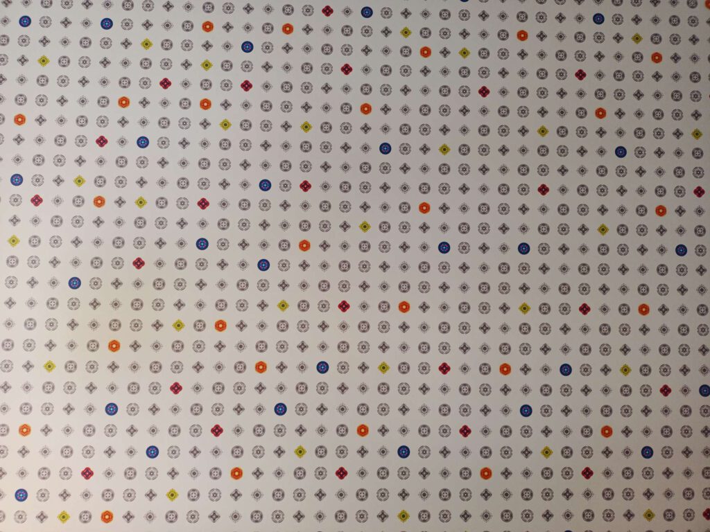 Op de wand zijn dezelfde symbolen gebruikt als op de vloer, in de kleuren grijs, blauw, rood, oranje en geel, met de verschillende tinten in die kleuren.