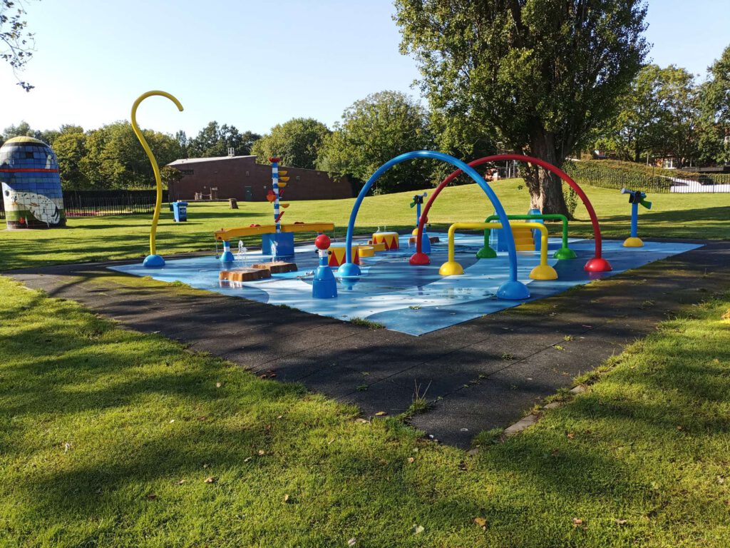 Een waterspeelplaats buiten met verschillende kleuren en attributen waar water uit komt.